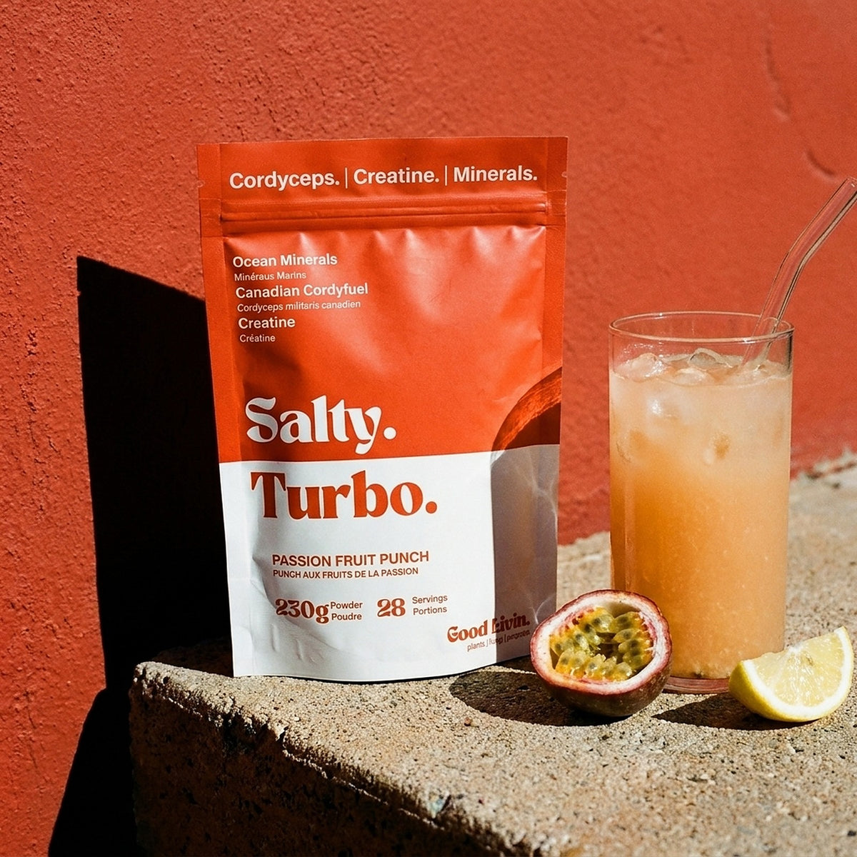 A bag of Salty Turbo passion fruit punch on a sunny concrete ledge next to a glass with ice, a halved passion fruit and a lemon wedge